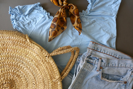 Fashionable outfit with blue ruffle blouse, worn out jeans, straw bag and leopard print scarf. Flat lay, gray background.の写真素材