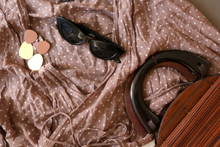 Fashionable outfit with blue nude dotted blouse, white skirt, vintage wooden bag, sunglasses and gold earrings. Flat lay, gray background.の写真素材