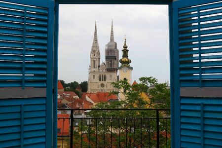 Panoramic view of Zagreb, Croatia with landmark Cathedral of the Assumption of the Blessed Virgin Mary and St. Mary Church through the decorative window frame in the front.の写真素材