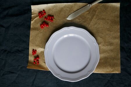 Table setting with navy tablecloth, parchment paper, one lilac plate, antique knife and red...