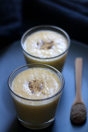 Two glasses of refreshing mango lassi drink, decorated with cardamom. Dark background, selective focus.の写真素材