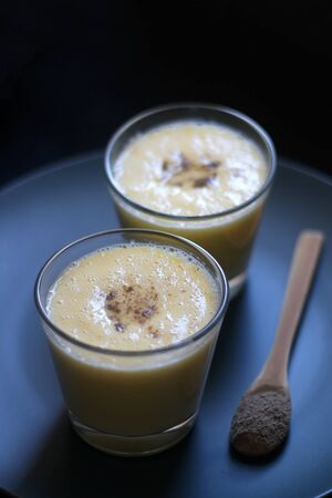 Two glasses of refreshing mango lassi drink, decorated with cardamom. Dark background, selective focus.の写真素材
