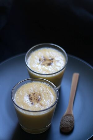 Two glasses of refreshing mango lassi drink, decorated with cardamom. Dark background, selective focus.の写真素材