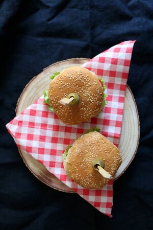 Two homemade vegan burgers made with chickpeas and zucchini, served with salad, tomato, cucumber, pickles and sauce. Top view, dark background.の写真素材