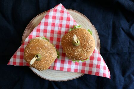 Two homemade vegan burgers made with chickpeas and zucchini, served with salad, tomato, cucumber, pickles and sauce. Top view, dark background.の写真素材