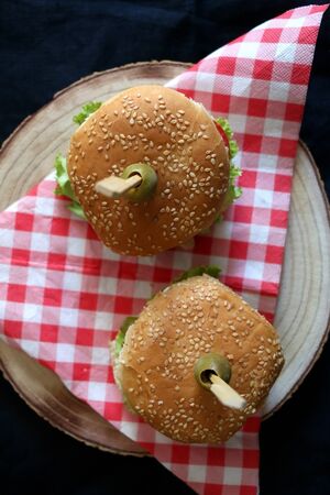 Two homemade vegan burgers made with chickpeas and zucchini, served with salad, tomato, cucumber, pickles and sauce. Top view, dark background.の写真素材