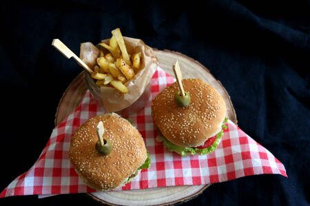 Two homemade vegan burgers made with chickpeas and zucchini, served with salad, tomato, cucumber, pickels and sauce. Fries on the side. Top view, dark background.の写真素材