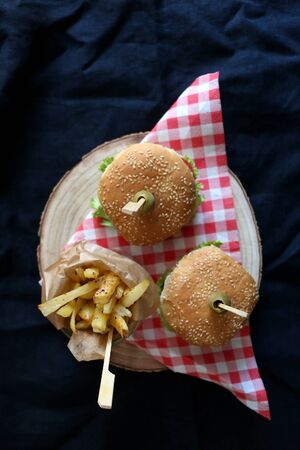Two homemade vegan burgers made with chickpeas and zucchini, served with salad, tomato, cucumber, pickels and sauce. Fries on the side. Top view, dark background.の写真素材
