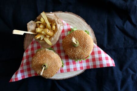 Two homemade vegan burgers made with chickpeas and zucchini, served with salad, tomato, cucumber, pickels and sauce. Fries on the side. Top view, dark background.の写真素材
