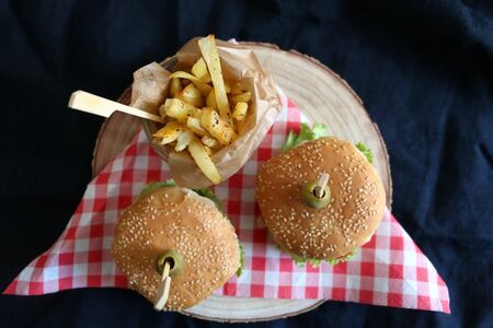 Two homemade vegan burgers made with chickpeas and zucchini, served with salad, tomato, cucumber, pickels and sauce. Fries on the side. Top view, dark background.の写真素材