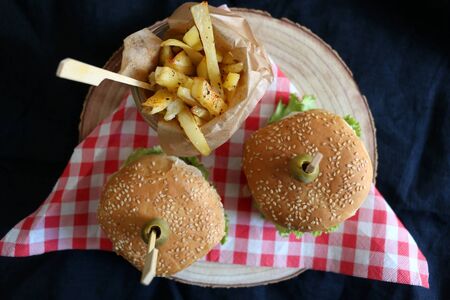 Two homemade vegan burgers made with chickpeas and zucchini, served with salad, tomato, cucumber, pickels and sauce. Fries on the side. Top view, dark background.の写真素材