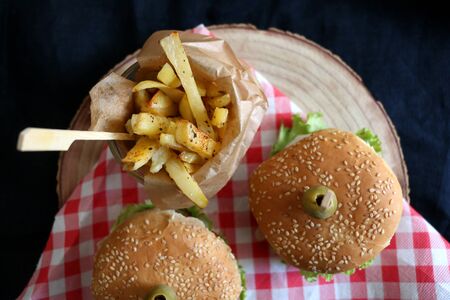 Two homemade vegan burgers made with chickpeas and zucchini, served with salad, tomato, cucumber, pickels and sauce. Fries on the side. Top view, dark background.の写真素材