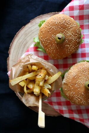 Two homemade vegan burgers made with chickpeas and zucchini, served with salad, tomato, cucumber, pickels and sauce. Fries on the side. Top view, dark background.の写真素材