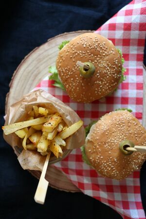 Two homemade vegan burgers made with chickpeas and zucchini, served with salad, tomato, cucumber, pickels and sauce. Fries on the side. Top view, dark background.の写真素材