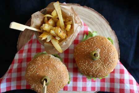Two homemade vegan burgers made with chickpeas and zucchini, served with salad, tomato, cucumber, pickels and sauce. Fries on the side. Top view, dark background.の写真素材