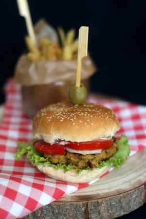 Homemade vegan burger made with chickpeas and zucchini, served with lettuce, tomato, cucumber, pickles and sauce. Fries on the side. Selective focus, dark background.の写真素材