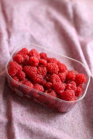 Fresh raspberries in a container. Selective focus, pink background.の写真素材