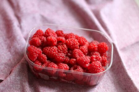 Fresh raspberries in a container. Selective focus, pink background.の写真素材