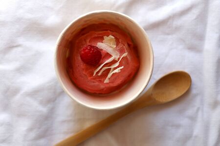 Strawberry vegan ice cream, decorated with raspberry and coconut flakes, in colorful paper cup. Top view.の写真素材