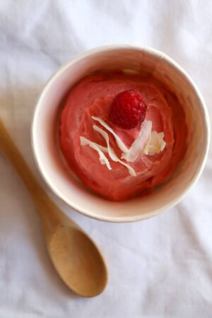 Strawberry vegan ice cream, decorated with raspberry and coconut flakes, in colorful paper cup. Top view.の写真素材