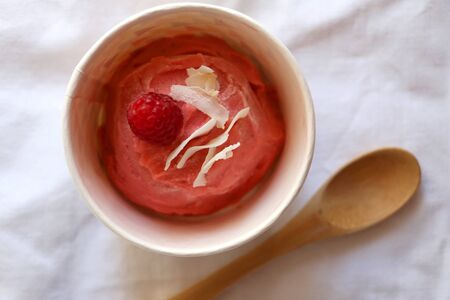 Strawberry vegan ice cream, decorated with raspberry and coconut flakes, in colorful paper cup. Top view.の写真素材