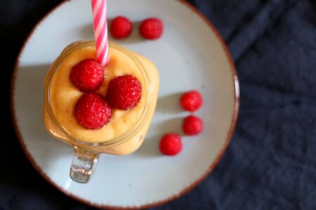 Mango and banana smoothie decorated with raspberries and reusable straw. Top view.の写真素材