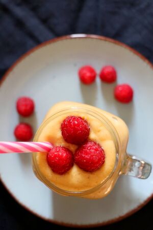 Mango and banana smoothie decorated with raspberries and reusable straw. Top view.の写真素材