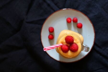Mango and banana smoothie decorated with raspberries and reusable straw. Top view.の写真素材