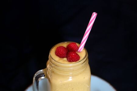 Mango and banana smoothie decorated with raspberries and reusable straw. Selective focus.の写真素材