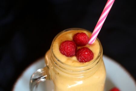 Mango and banana smoothie decorated with raspberries and reusable straw. Selective focus.の写真素材