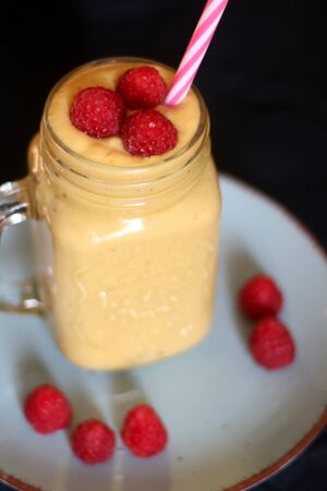 Mango and banana smoothie decorated with raspberries and reusable straw. Selective focus.の写真素材