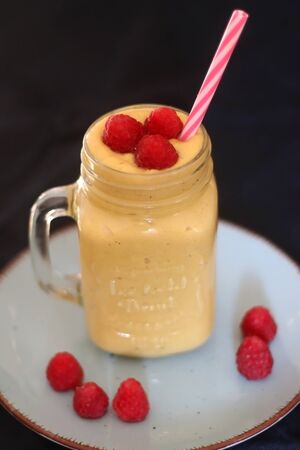 Mango and banana smoothie decorated with raspberries and reusable straw. Selective focus.の写真素材