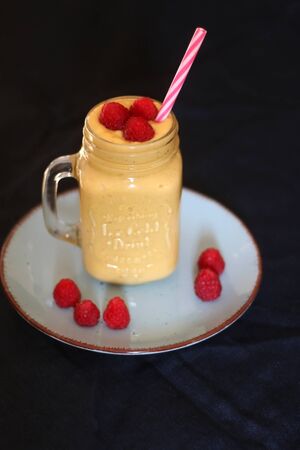 Mango and banana smoothie decorated with raspberries and reusable straw. Selective focus.の写真素材