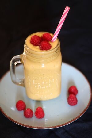 Mango and banana smoothie decorated with raspberries and reusable straw. Selective focus.の写真素材