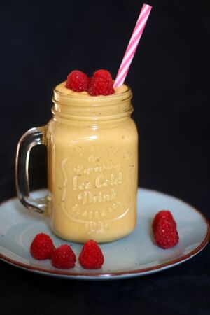 Mango and banana smoothie decorated with raspberries and reusable straw. Selective focus.の写真素材