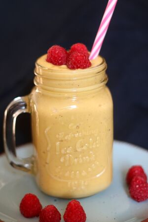 Mango and banana smoothie decorated with raspberries and reusable straw. Selective focus.の写真素材