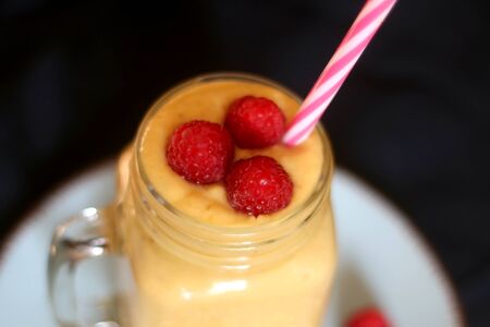 Mango and banana smoothie decorated with raspberries and reusable straw. Selective focus.の写真素材