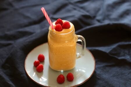 Mango and banana smoothie decorated with raspberries and reusable straw. Selective focus.の写真素材