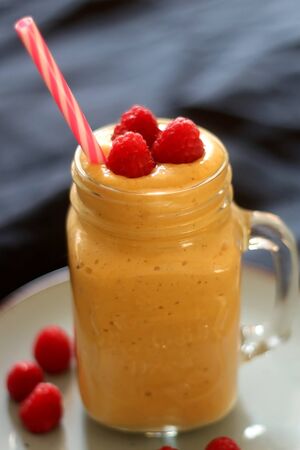 Mango and banana smoothie decorated with raspberries and reusable straw. Selective focus.の写真素材