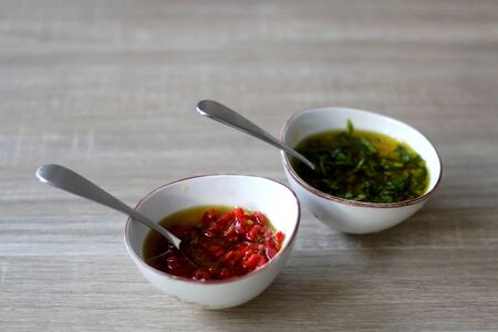 Two small bowls of olive oil sauce, one with chili pepper and one with basil. Selective focus.の写真素材