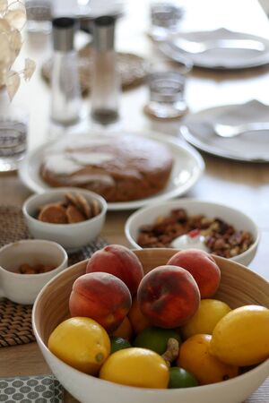 Bowl of fruit (peach, lemon, lime) served on a table, with desserts and nuts in the background. Selective focus.の写真素材