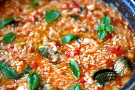 Orzo pasta, cooked with tomato sauce, vegetables and seafood, served on a table. Selective focus.の写真素材