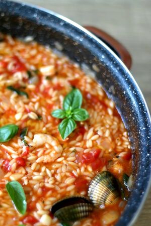 Orzo pasta, cooked with tomato sauce, vegetables and seafood, served on a table. Selective focus.の写真素材