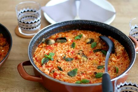 Orzo pasta, cooked with tomato sauce, vegetables and seafood, served on a table. Selective focus.の写真素材