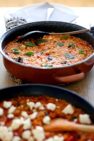 Two pots of orzo pasta, with tomato sauceand vegetables. One with seafood, one vegetarian with feta cheese, served on a table. Selective focus.の写真素材