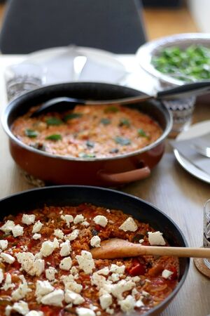Two pots of orzo pasta, with tomato sauceand vegetables. One with seafood, one vegetarian with feta cheese, served on a table. Selective focus.の写真素材
