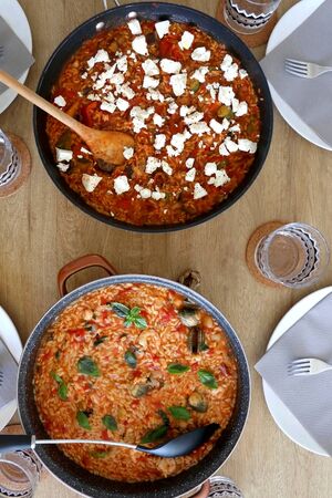 Two pots of orzo pasta, with tomato sauceand vegetables. One with seafood, one vegetarian with feta cheese, served on a table. Top view.の写真素材