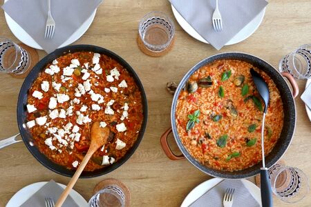 Two pots of orzo pasta, with tomato sauceand vegetables. One with seafood, one vegetarian with feta cheese, served on a table. Top view.の写真素材