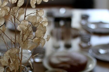 Vase with dry flowers on the table, with dishware and served food in the background. Selective focus.の写真素材