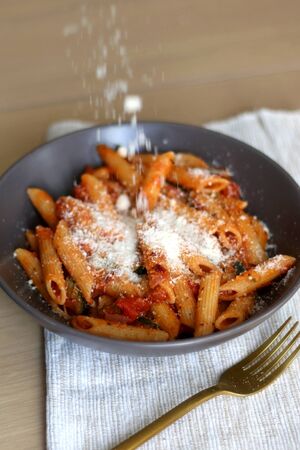 Sprinkling parmesan cheese on a plate of pasta with tomato sauce and eggplant. Selective focus.の写真素材